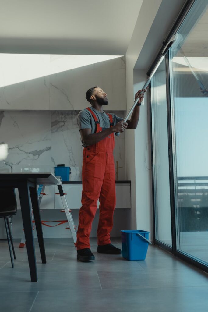 pexels photo 6197122 6197122 A man in coveralls cleans a large window in a stylish, modern home interior.